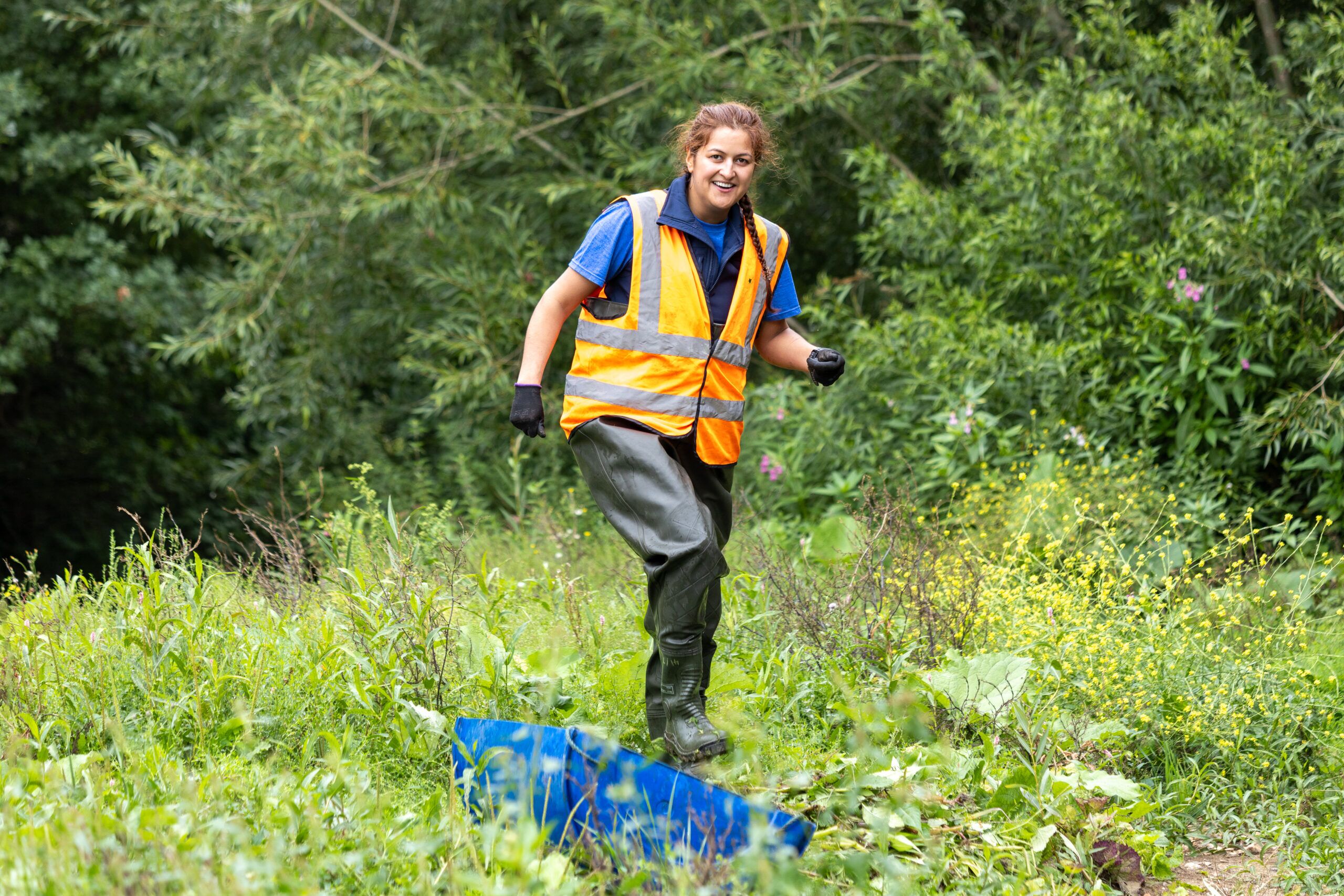 A female volunteer in a high vis vest at a river clean up event.